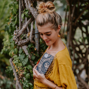 Woman in a yellow top holding a patterned clutch in front of greenery